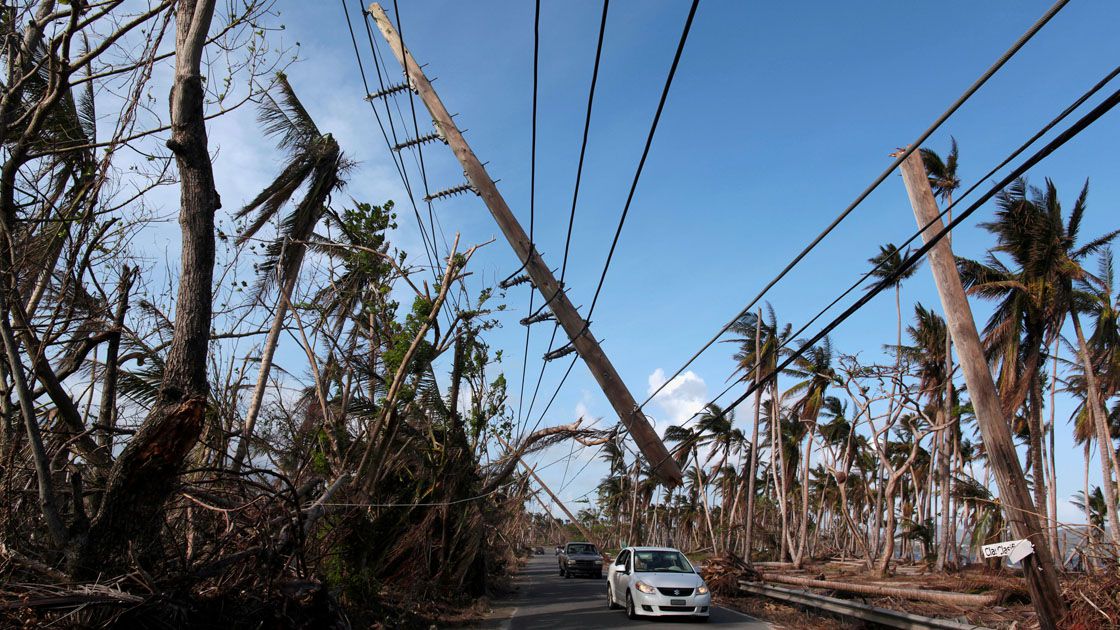 FILE PHOTO: Cars drive under a partially collapsed utility pole, after the island was hit by Hurricane Maria in September, in Naguabo