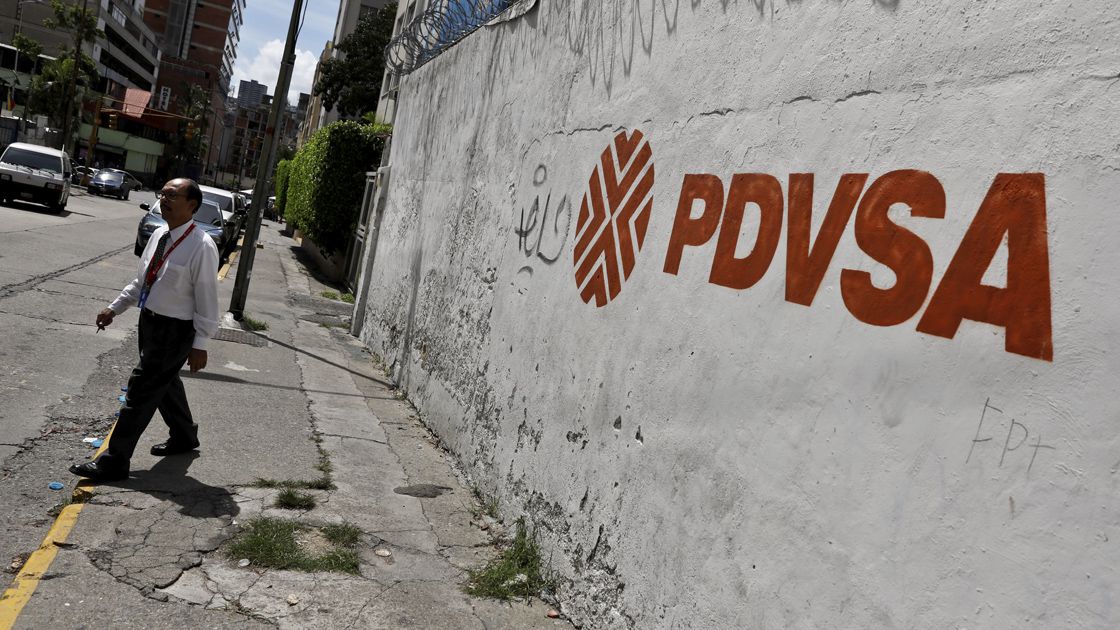 A man walks past a mural with the corporate logo of the state oil company PDVSA in Caracas