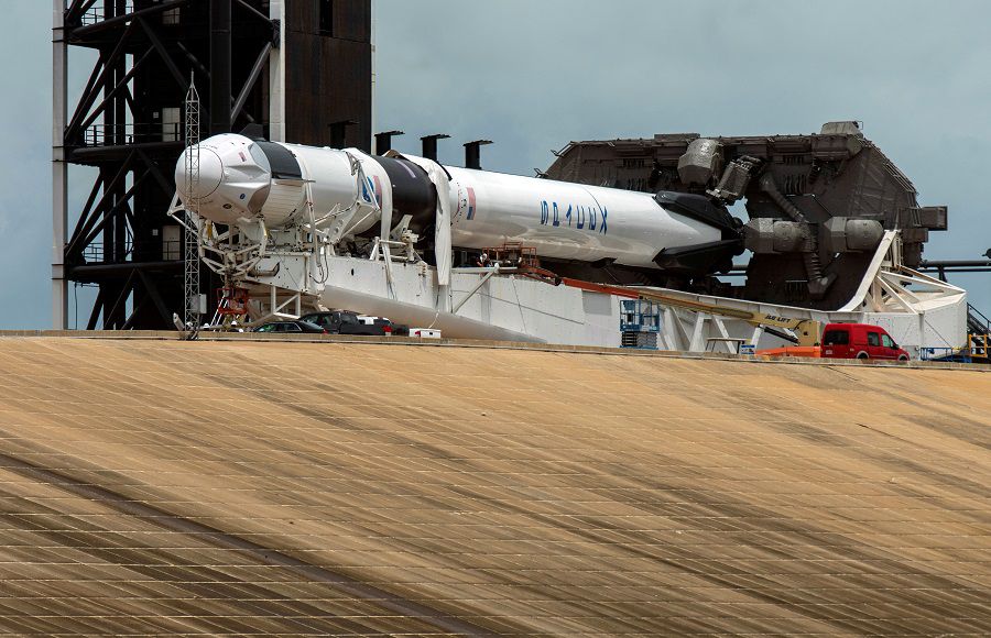 Crews work on the SpaceX Crew Dragon, attached to a Falcon 9 booster rocket, as it sits horizontal on Pad39A