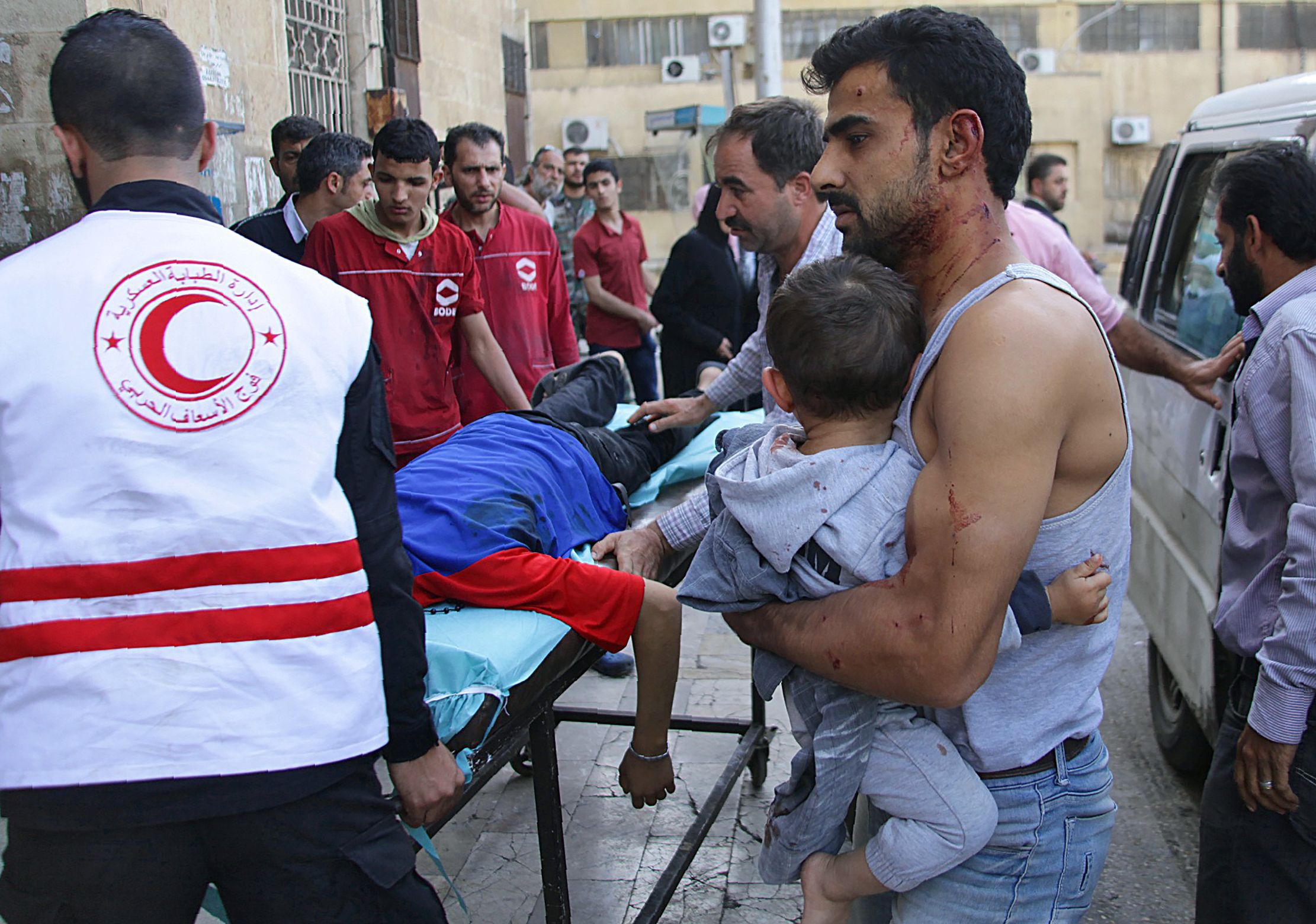 A Syrian man carries a child as they await treatment at a hospital in