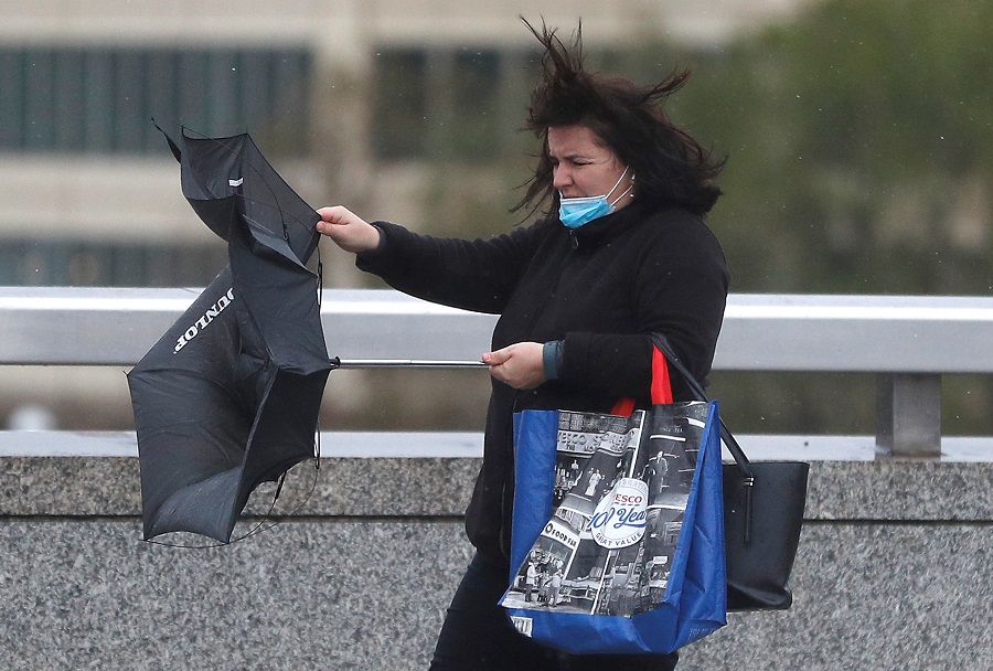 A woman struggles with an umbrella as she crosses London Bridge in strong winds and rain, in London