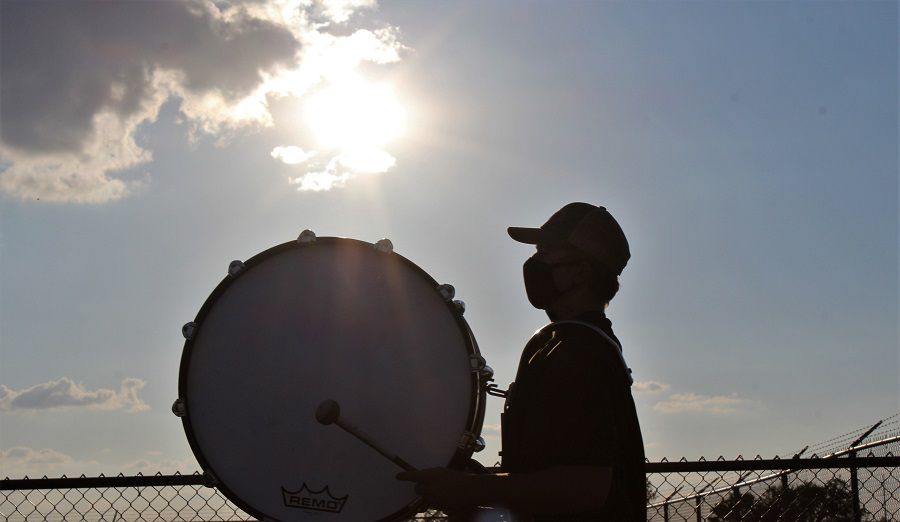 A Clyde High School drummer, wearing a face mask, is silhouetted against the setting sun before Friday's game against Idalou.