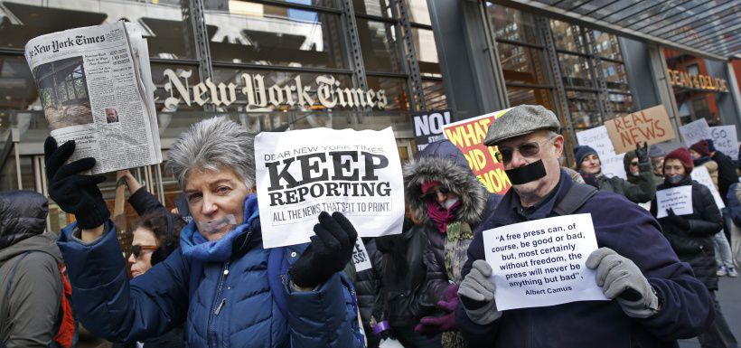 People with taped mouths hold signs and a copy of the New York Times