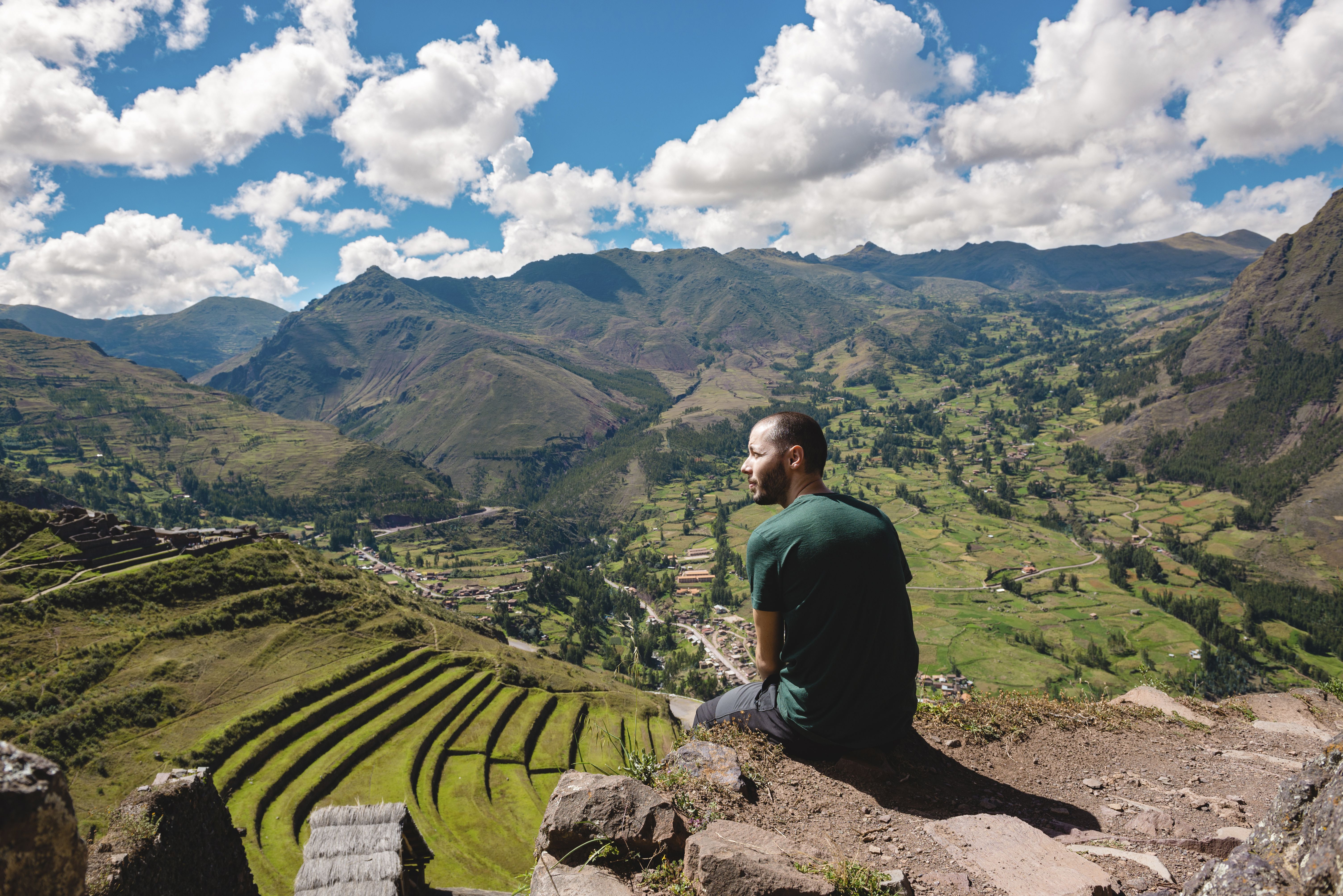 Rear view of hiker looking at view while sitting on mountain against sky at Pisac