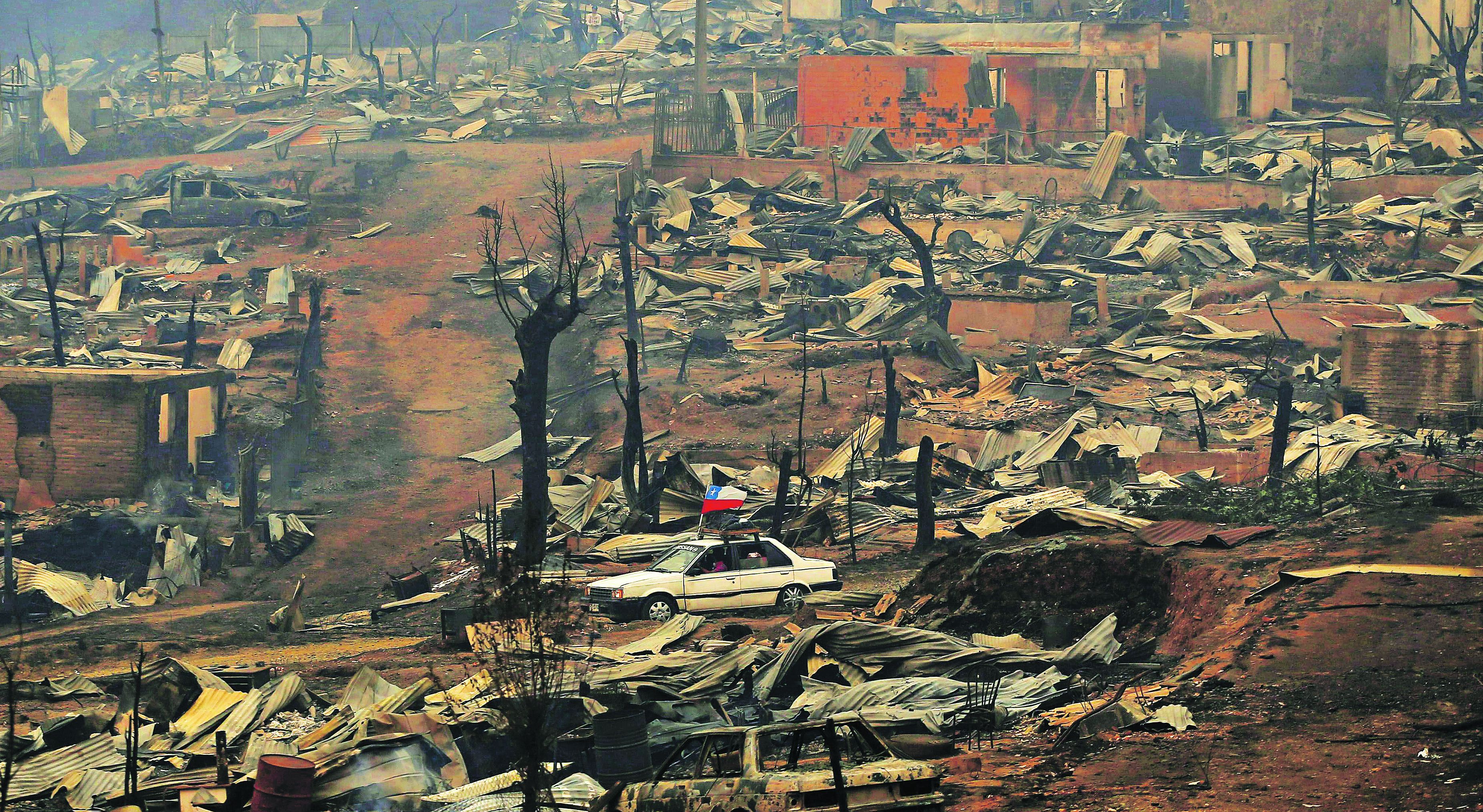 A car with a Chilean flag drives through the debris after a forest fi