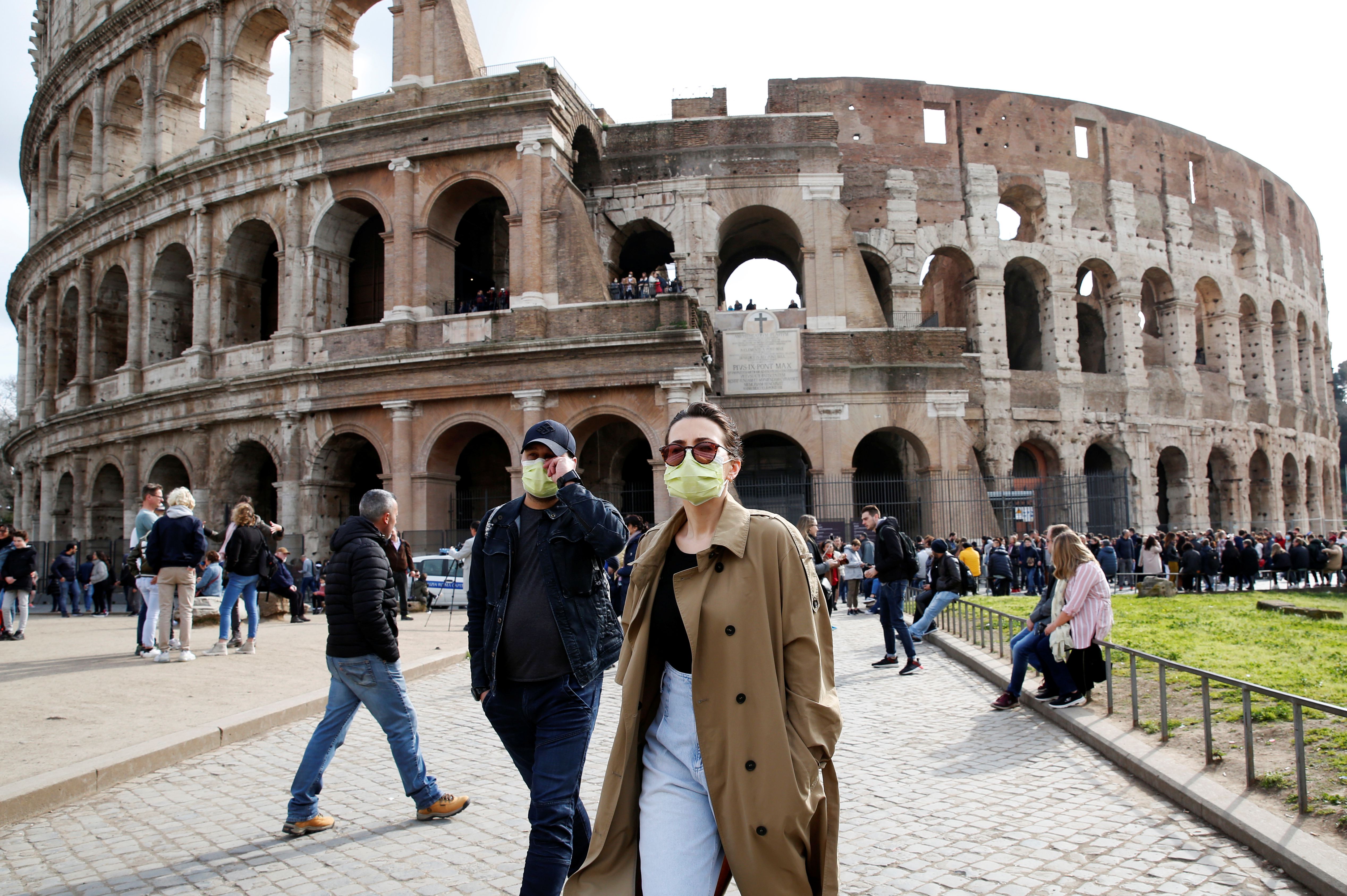 People wearing protective masks walk past the Colosseum in Rome