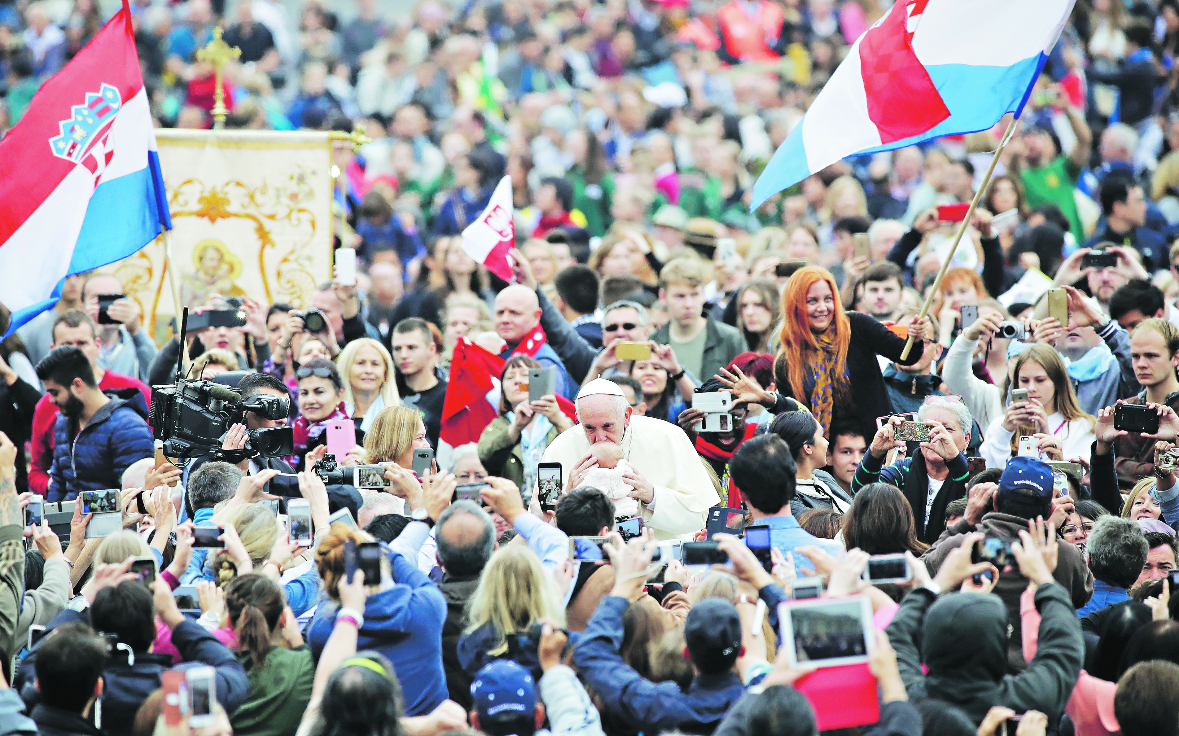 Pope Francis kisses a baby as Croatian flags are waved by pilgrims at