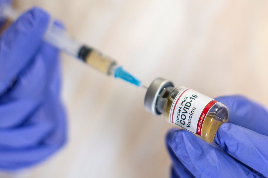 A woman holds a small bottle labeled with a "Coronavirus COVID-19 Vaccine" sticker and a medical syringe in this illustration