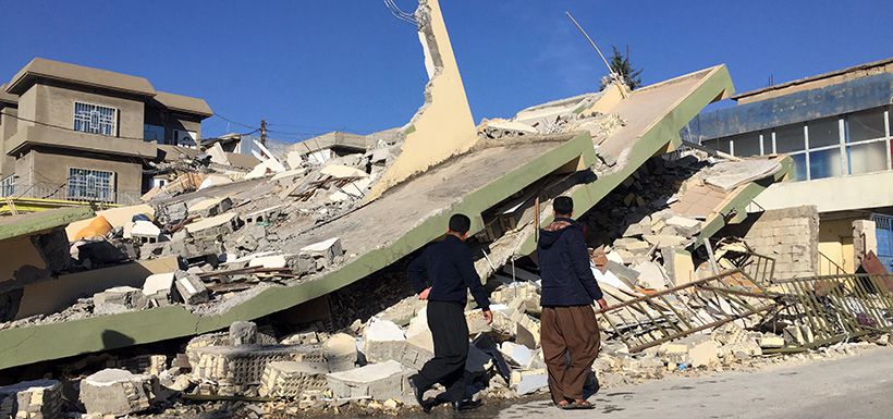 People walk past a damaged building following an earthquake in Darbandikhan