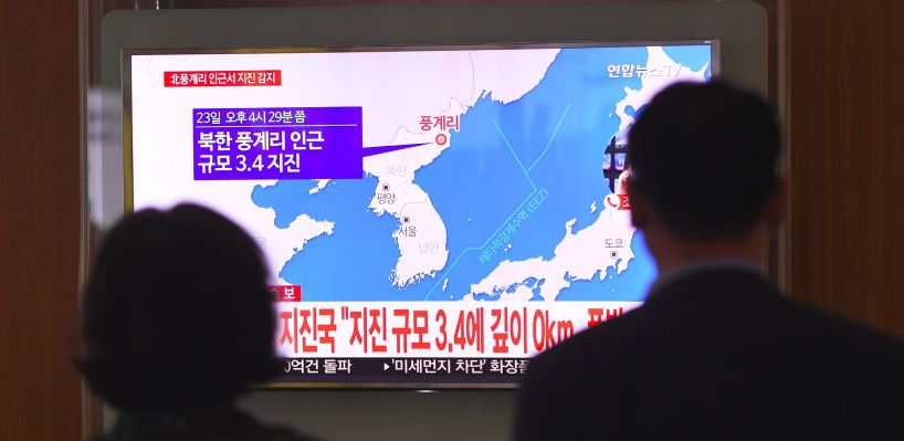 People watch a television news screen showing a map of the epicenter